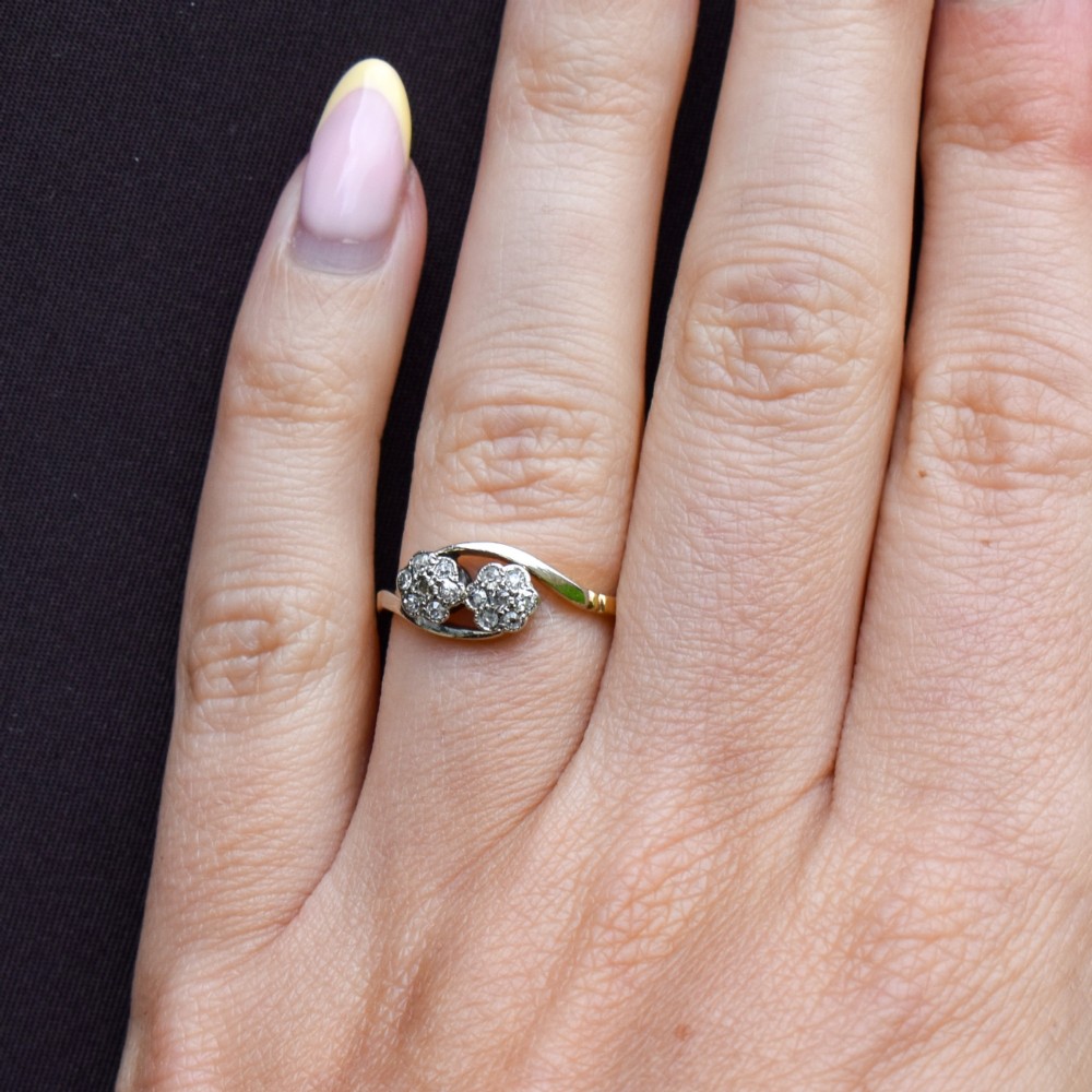 An antique 18ct yellow gold crossover ring featuring two diamond cluster flowers set in white metal on sweeping twist shoulders. View X