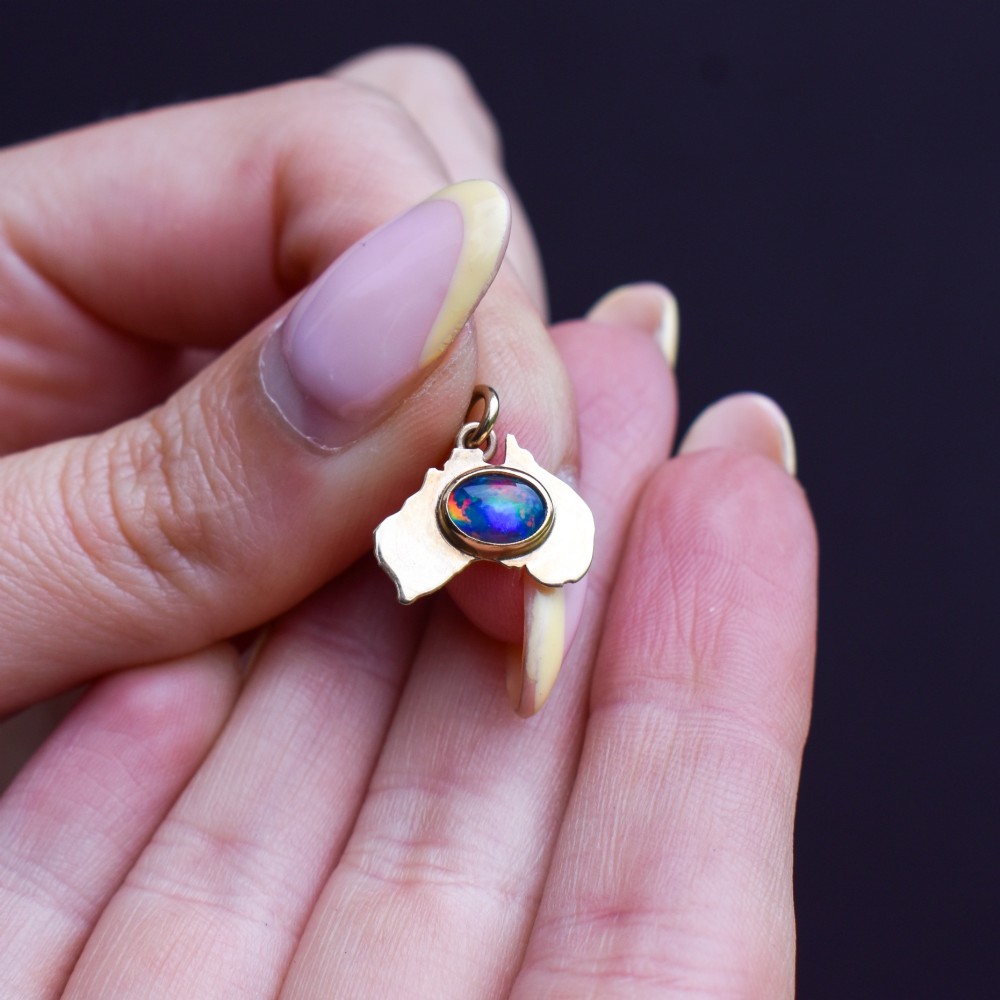 A 9ct yellow gold pendant in the shape of Australia, featuring a central bezel-set oval black opal triplet with blue and violet play-of-colour. View VIII