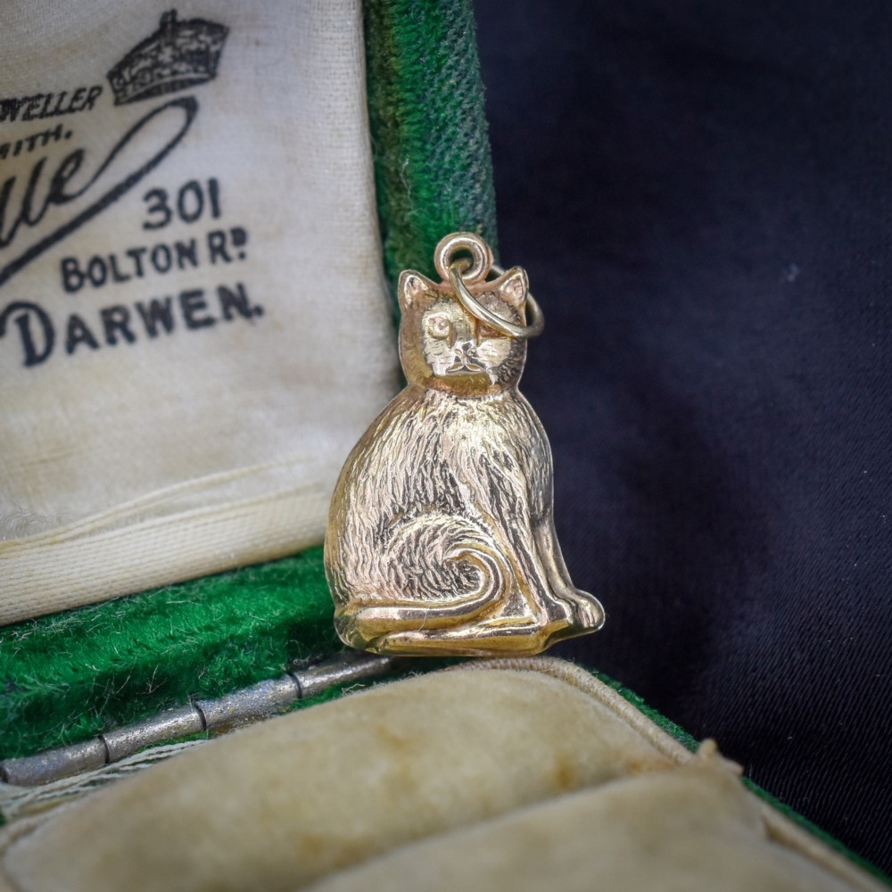 A small 9ct yellow gold charm shaped as a seated cat with engraved fur texture and a loop at the top for suspension.