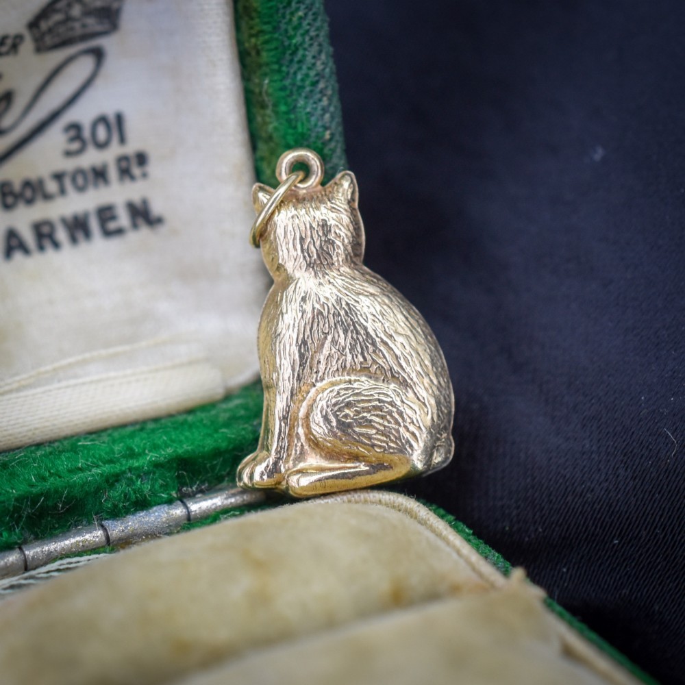 A small 9ct yellow gold charm shaped as a seated cat with engraved fur texture and a loop at the top for suspension. View III