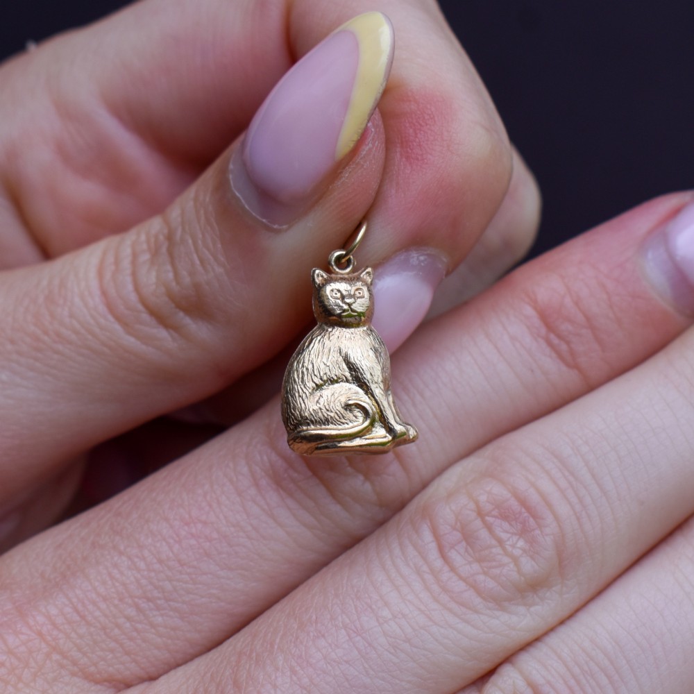A small 9ct yellow gold charm shaped as a seated cat with engraved fur texture and a loop at the top for suspension. View VIII