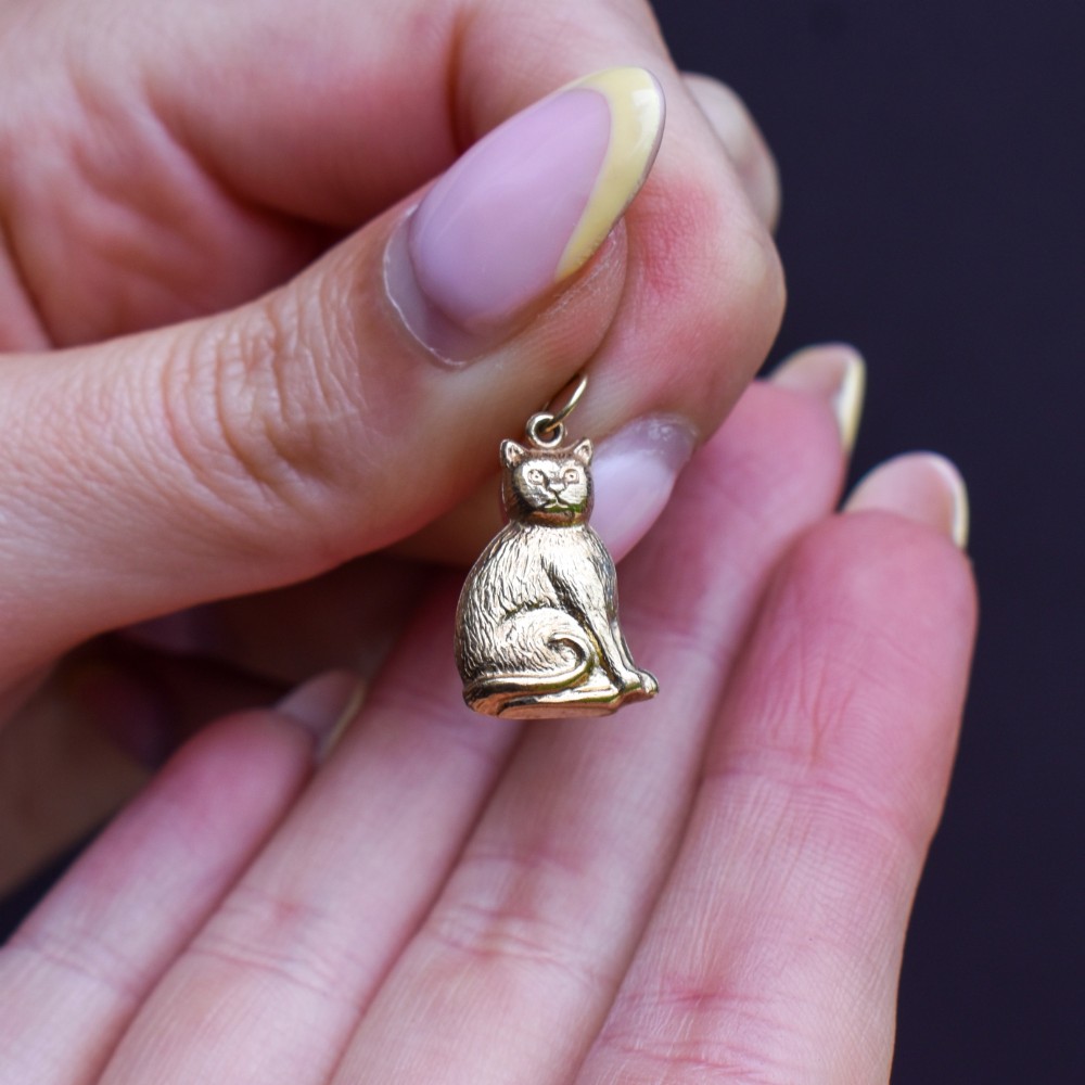 A small 9ct yellow gold charm shaped as a seated cat with engraved fur texture and a loop at the top for suspension. View IX