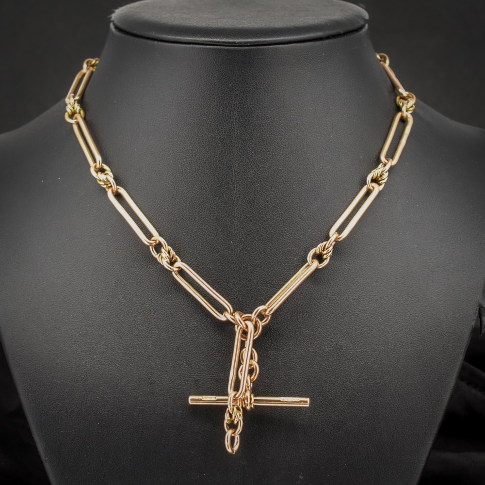 An antique 9ct yellow gold necklace featuring elongated trombone links, twisted love knots, and a central suspended T-bar.