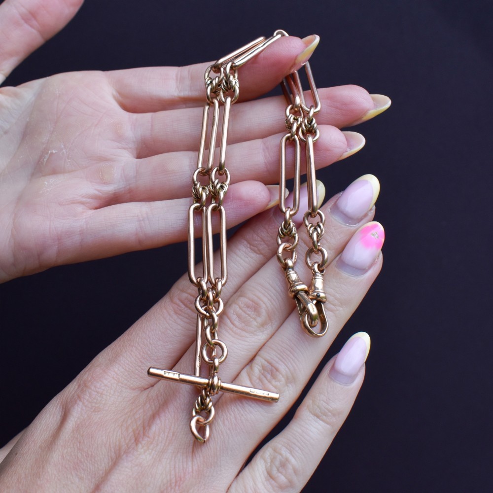An antique 9ct yellow gold necklace featuring elongated trombone links, twisted love knots, and a central suspended T-bar. View X