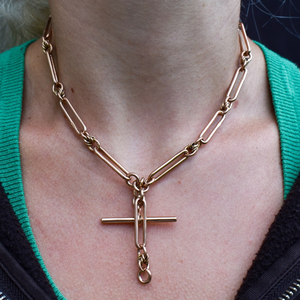 An antique 9ct yellow gold necklace featuring elongated trombone links, twisted love knots, and a central suspended T-bar. View XI