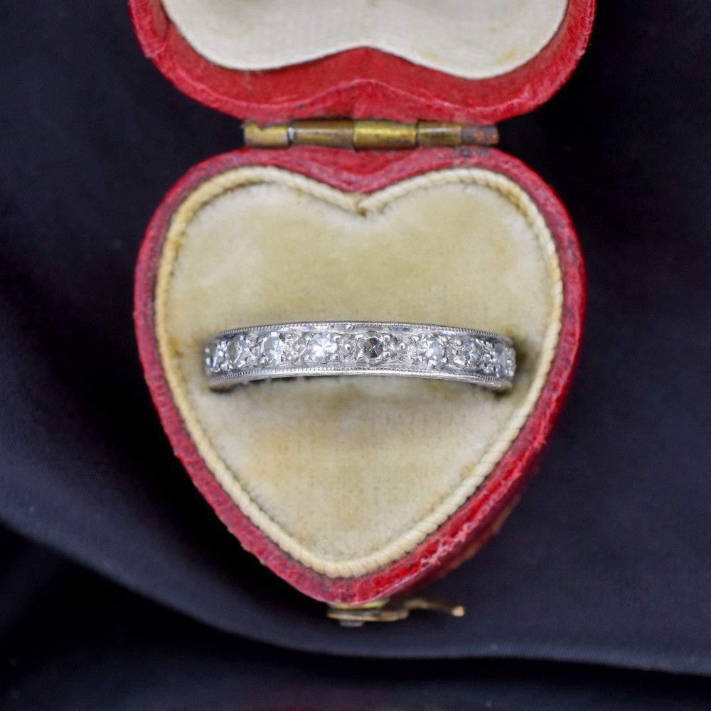 An Art Deco palladium full eternity ring set with a continuous band of round diamonds bordered by milgrain edging.