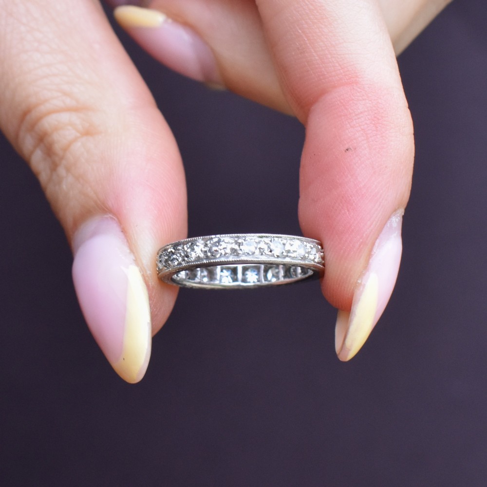 An Art Deco palladium full eternity ring set with a continuous band of round diamonds bordered by milgrain edging. View VIII