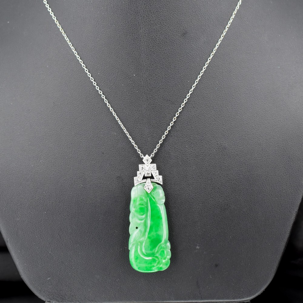An Art Deco carved green jade pendant with geometric platinum and diamond accents on a chain.