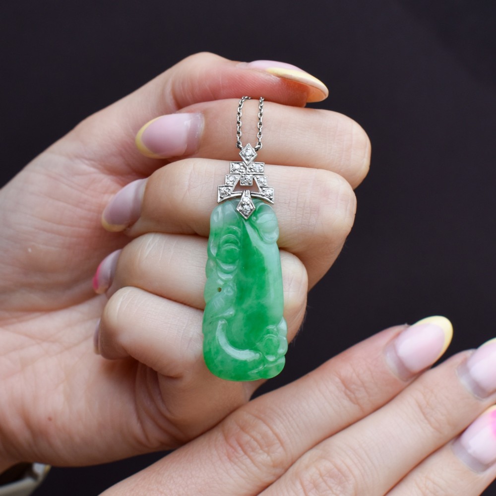 An Art Deco carved green jade pendant with geometric platinum and diamond accents on a chain. View IX