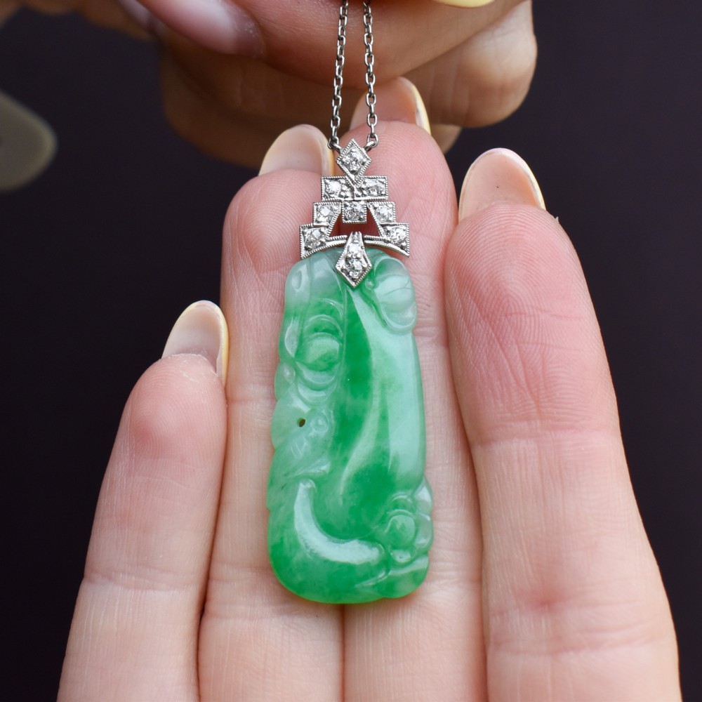 An Art Deco carved green jade pendant with geometric platinum and diamond accents on a chain. View X