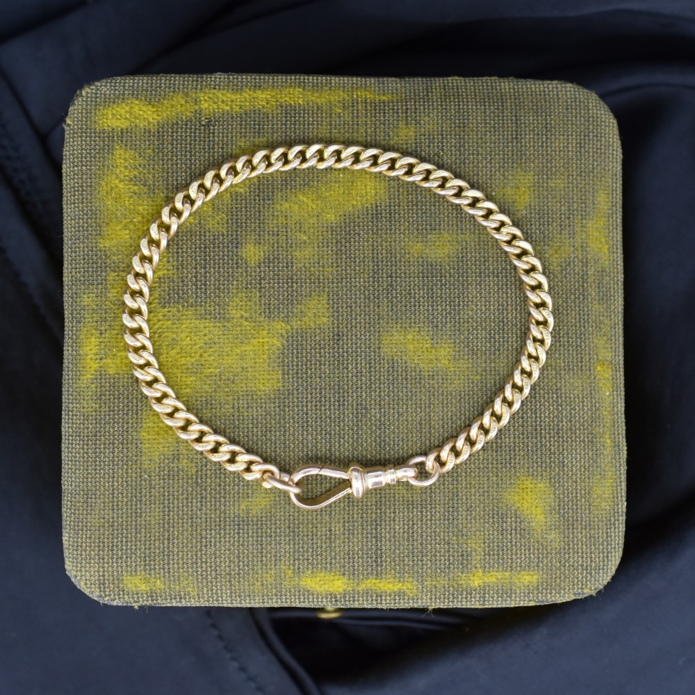 An antique 9ct yellow gold uniform curb link chain bracelet with a dog clip clasp arrangement resting on a textured olive display pad.
