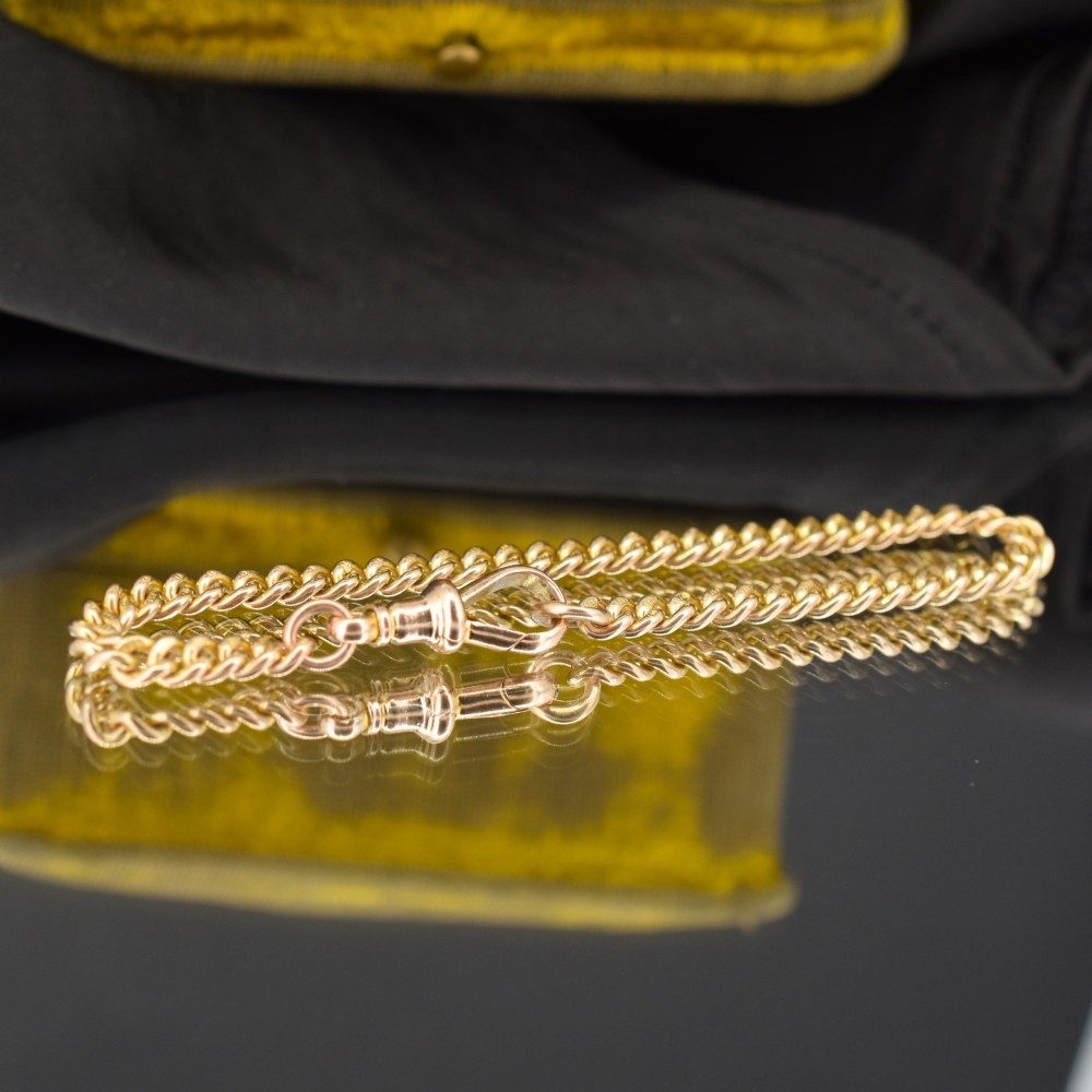 An antique 9ct yellow gold uniform curb link chain bracelet with a dog clip clasp arrangement resting on a textured olive display pad. View IV