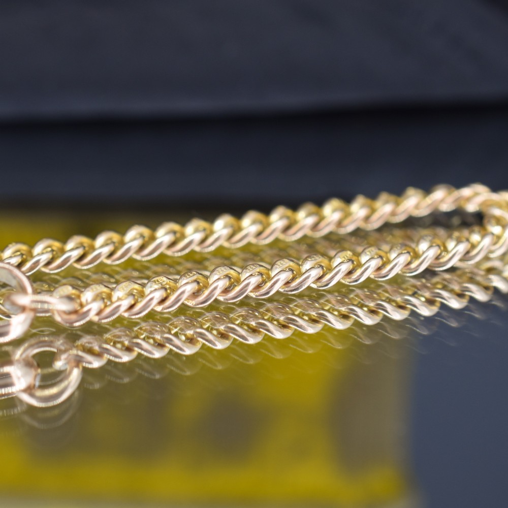 An antique 9ct yellow gold uniform curb link chain bracelet with a dog clip clasp arrangement resting on a textured olive display pad. View V