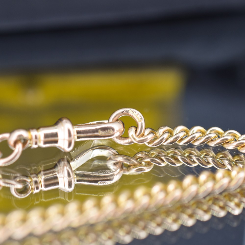 An antique 9ct yellow gold uniform curb link chain bracelet with a dog clip clasp arrangement resting on a textured olive display pad. View VI