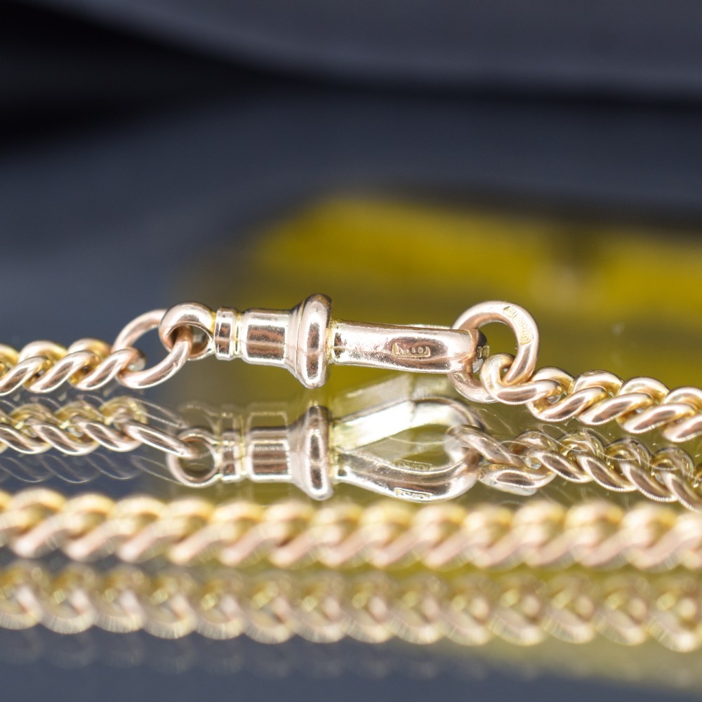 An antique 9ct yellow gold uniform curb link chain bracelet with a dog clip clasp arrangement resting on a textured olive display pad. View VII