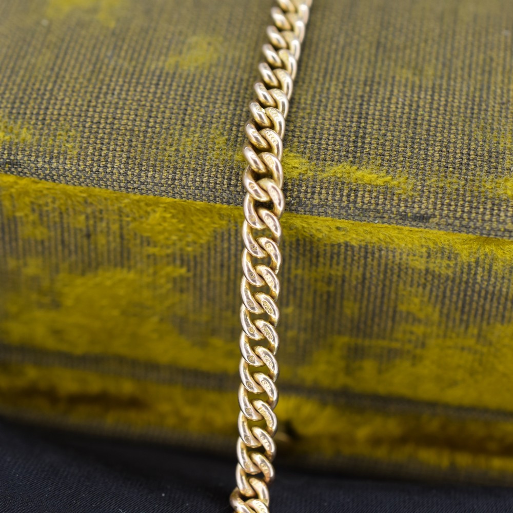 An antique 9ct yellow gold uniform curb link chain bracelet with a dog clip clasp arrangement resting on a textured olive display pad. View VIII