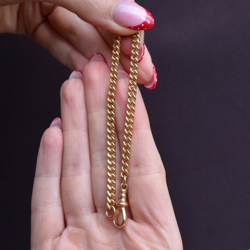 An antique 9ct yellow gold uniform curb link chain bracelet with a dog clip clasp arrangement resting on a textured olive display pad. View IX