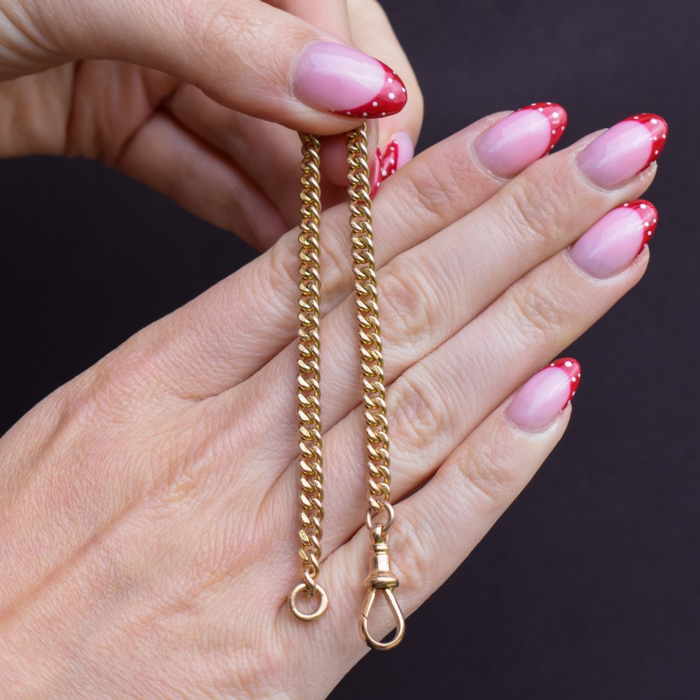 An antique 9ct yellow gold uniform curb link chain bracelet with a dog clip clasp arrangement resting on a textured olive display pad. View X