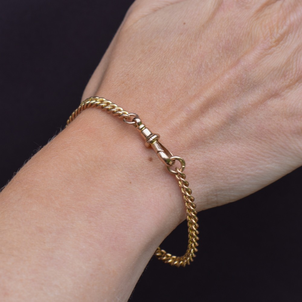 An antique 9ct yellow gold uniform curb link chain bracelet with a dog clip clasp arrangement resting on a textured olive display pad. View XI