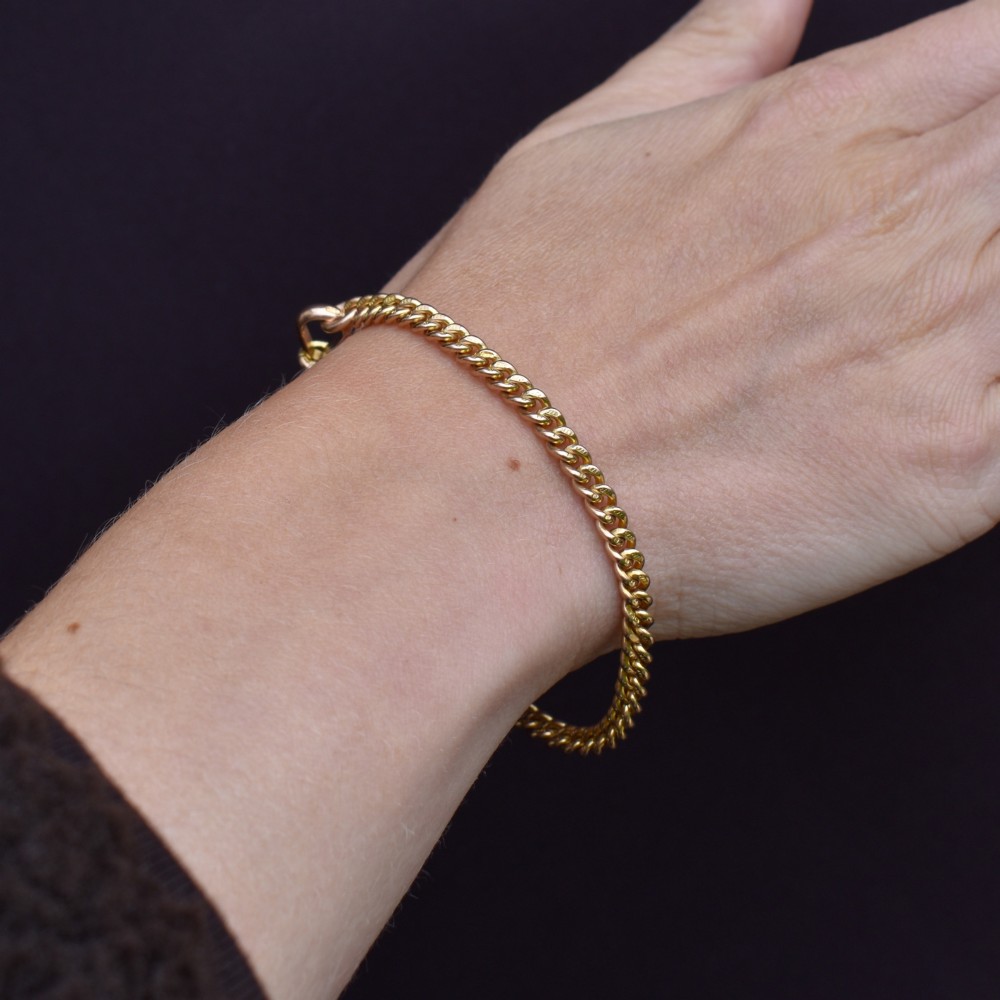 An antique 9ct yellow gold uniform curb link chain bracelet with a dog clip clasp arrangement resting on a textured olive display pad. View XII