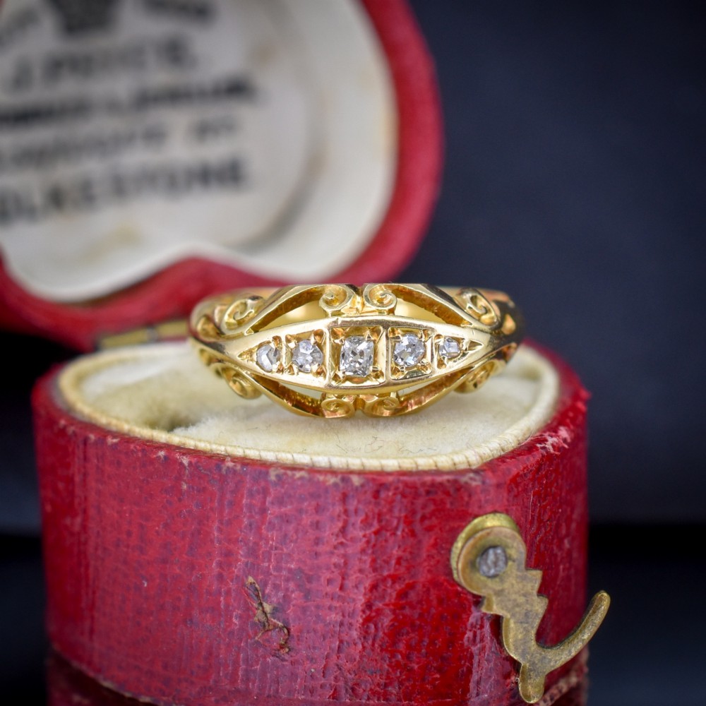 An 18ct yellow gold boat-shaped ring set with five graduated diamonds and featuring carved scrollwork along the gallery.