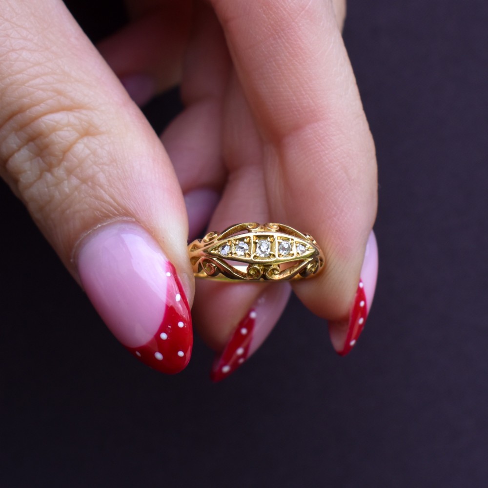 An 18ct yellow gold boat-shaped ring set with five graduated diamonds and featuring carved scrollwork along the gallery. View IX