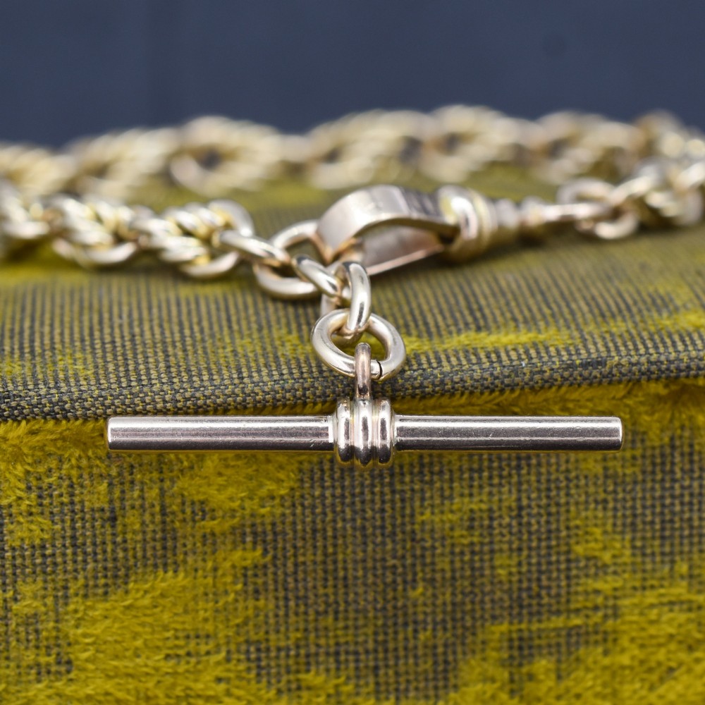 An Edwardian 9ct yellow gold love knot chain bracelet with a suspended T-bar and swivel clasp fastener on a textured green surface. View II