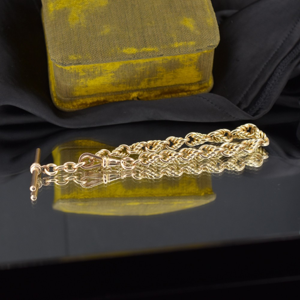 An Edwardian 9ct yellow gold love knot chain bracelet with a suspended T-bar and swivel clasp fastener on a textured green surface. View III