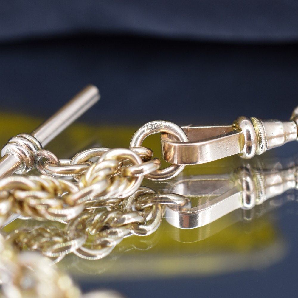 An Edwardian 9ct yellow gold love knot chain bracelet with a suspended T-bar and swivel clasp fastener on a textured green surface. View IV