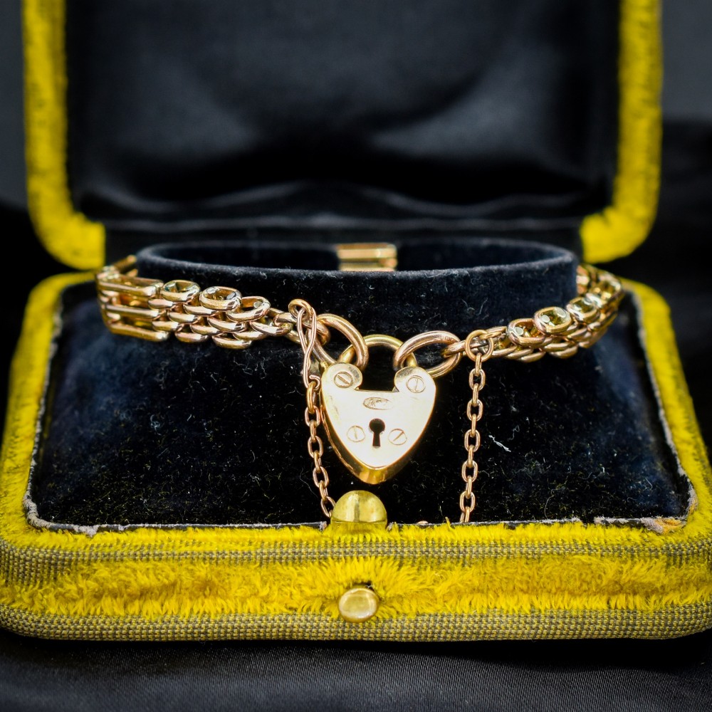 An antique rolled gold gate link bracelet featuring an engraved heart-shaped padlock clasp and safety chain.