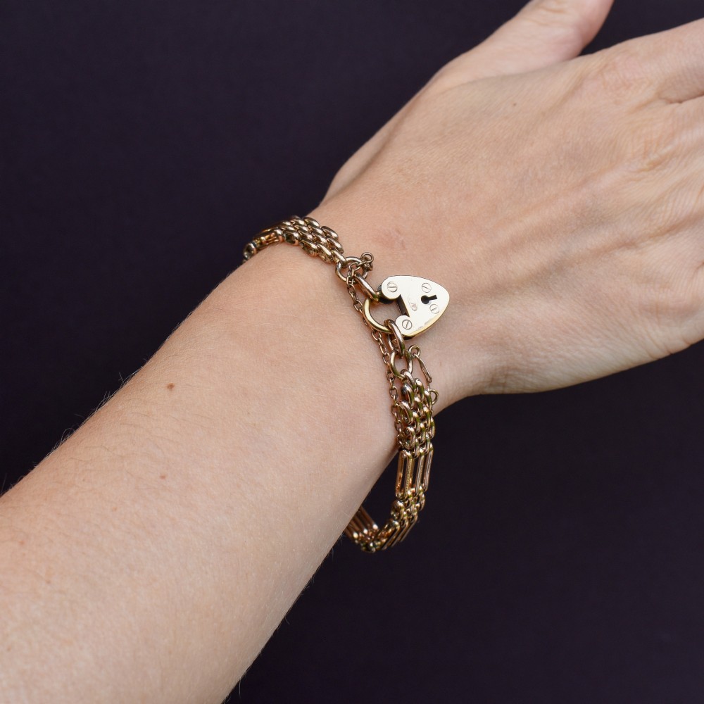 An antique rolled gold gate link bracelet featuring an engraved heart-shaped padlock clasp and safety chain. View IX