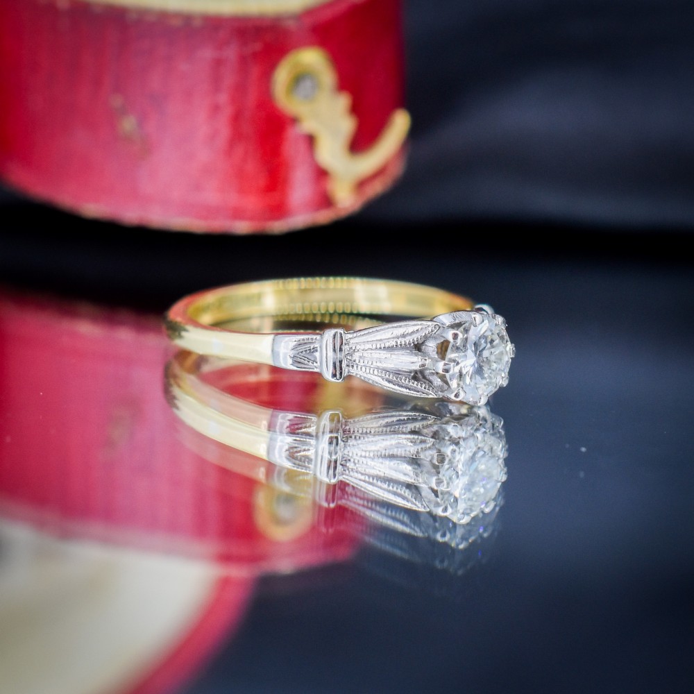 An Art Deco diamond solitaire ring featuring a round cut diamond set between detailed, fan-etched shoulders on an 18ct yellow gold band. View V