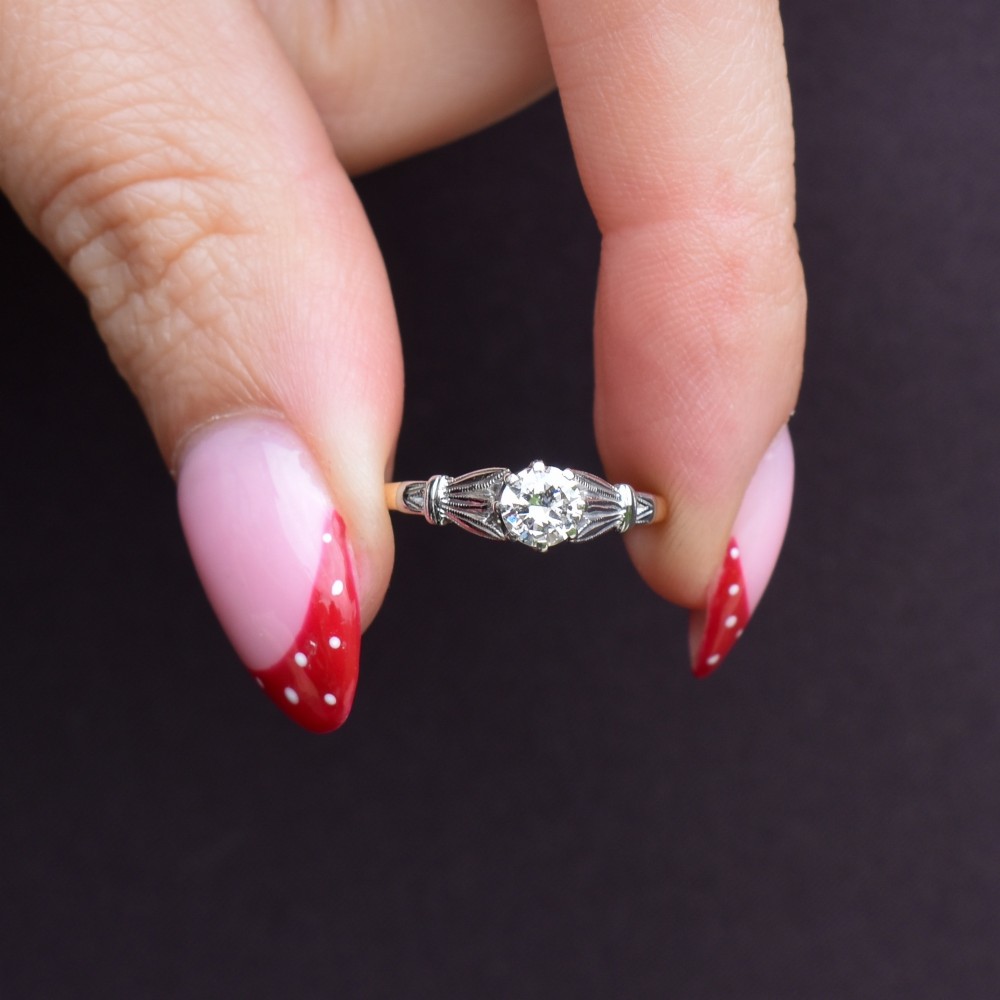 An Art Deco diamond solitaire ring featuring a round cut diamond set between detailed, fan-etched shoulders on an 18ct yellow gold band. View X