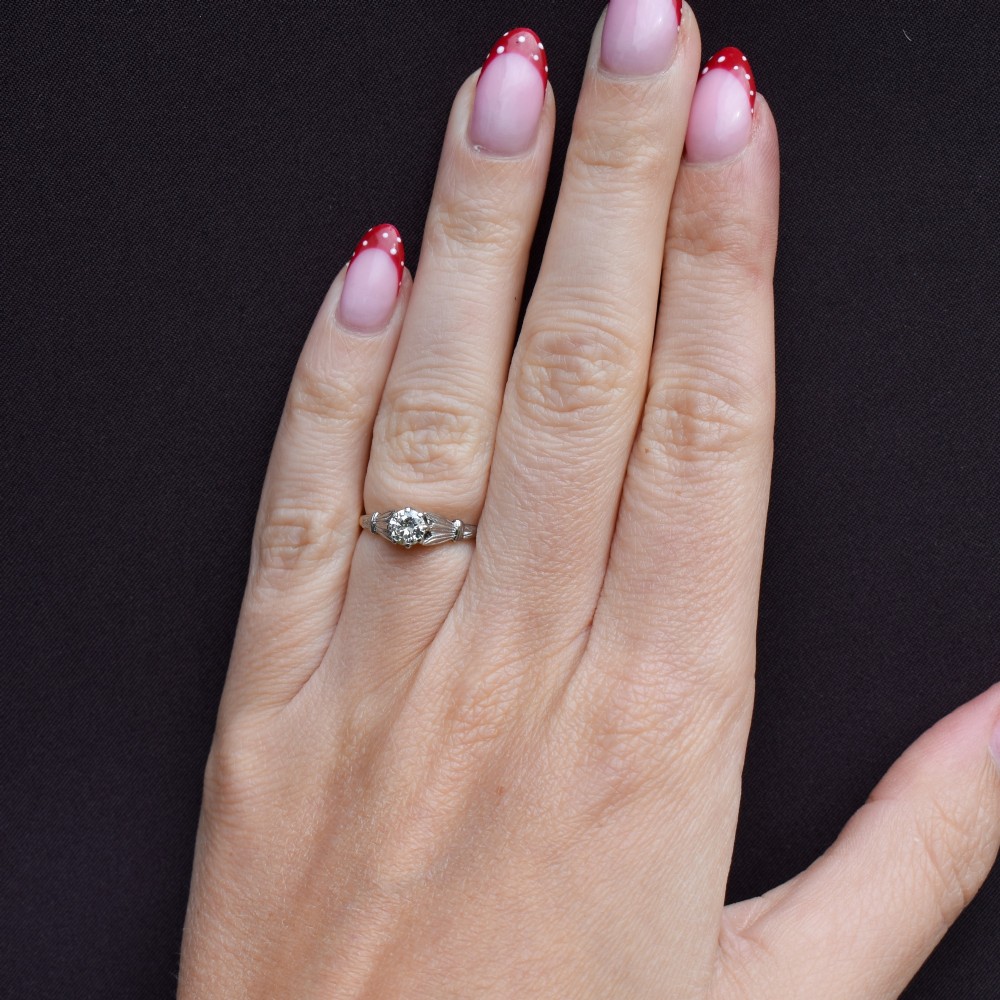 An Art Deco diamond solitaire ring featuring a round cut diamond set between detailed, fan-etched shoulders on an 18ct yellow gold band. View XI