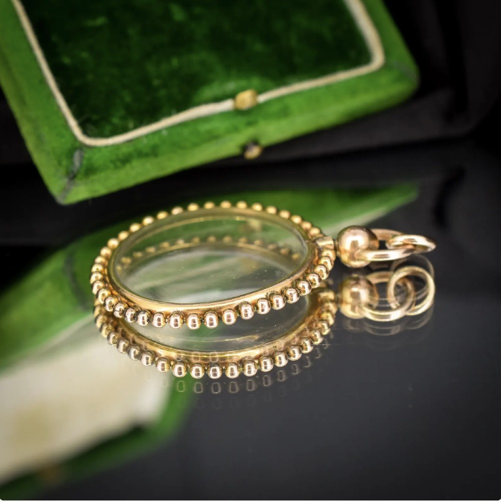 A circular antique gold locket featuring clear glass panels surrounded by a beaded metal border and attached to a suspension loop. View VIII