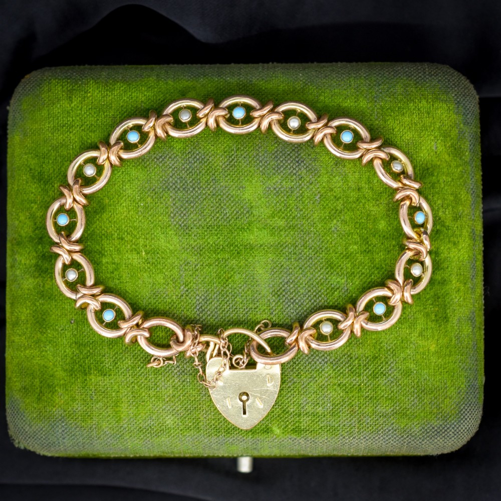 An antique rolled gold chain bracelet inset with alternating seed pearls and turquoise cabochons, featuring a heart-shaped padlock clasp with safety chain.
