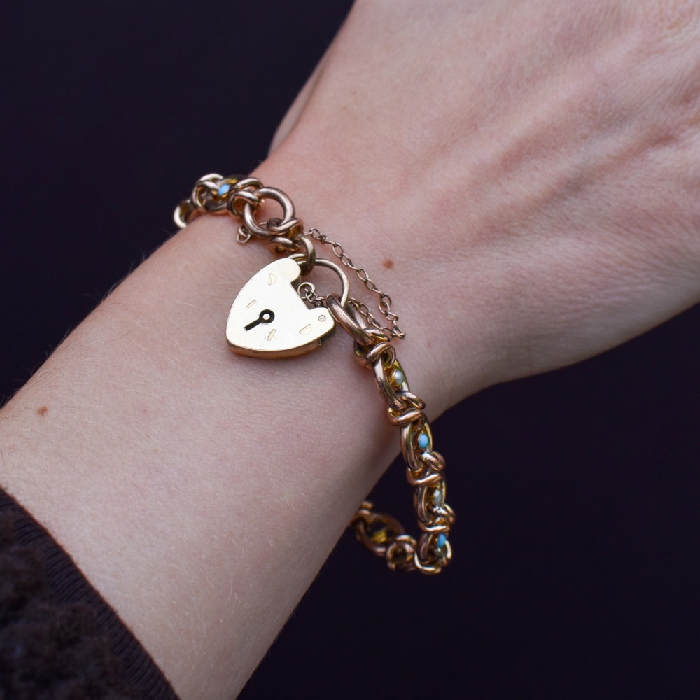 An antique rolled gold chain bracelet inset with alternating seed pearls and turquoise cabochons, featuring a heart-shaped padlock clasp with safety chain. View IX