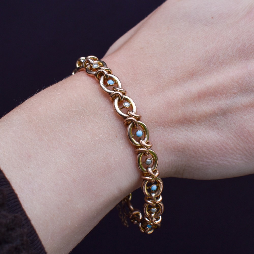 An antique rolled gold chain bracelet inset with alternating seed pearls and turquoise cabochons, featuring a heart-shaped padlock clasp with safety chain. View X