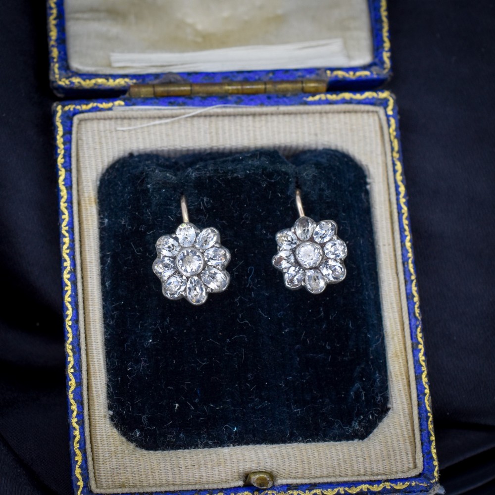 A pair of antique Georgian flower-shaped cluster earrings featuring clear paste stones set in silver with gold ear wires.