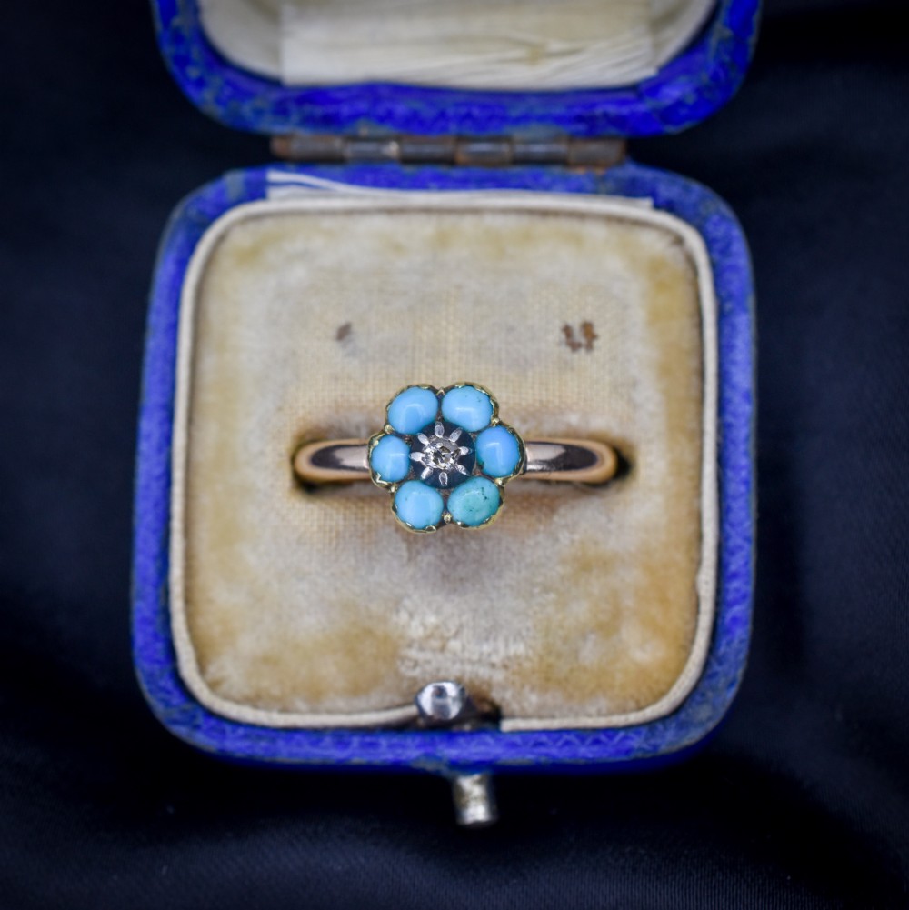 An antique 15ct yellow gold ring featuring a central diamond surrounded by six turquoise cabochons forming a floral cluster.