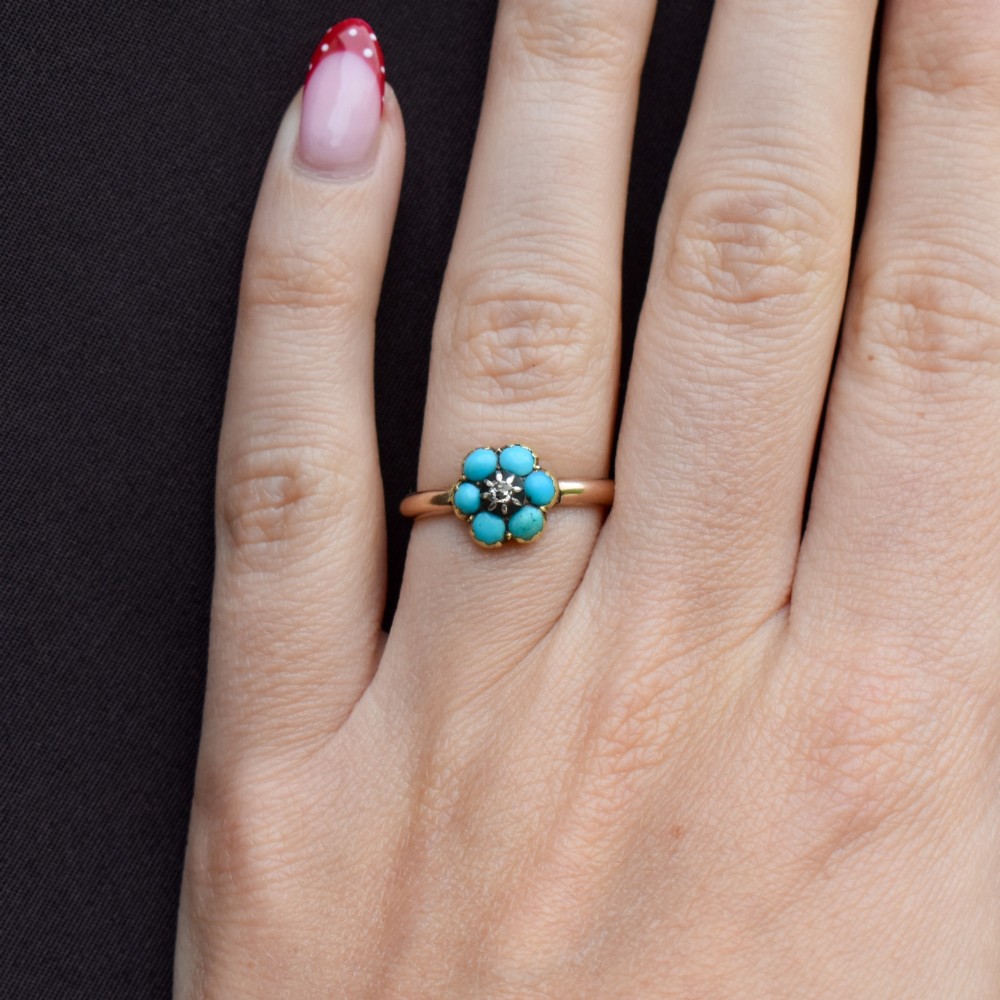 An antique 15ct yellow gold ring featuring a central diamond surrounded by six turquoise cabochons forming a floral cluster. View X
