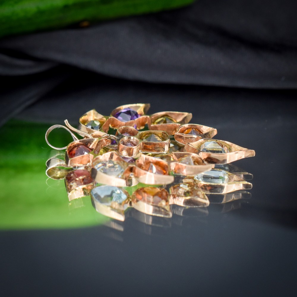 An antique 9ct yellow gold floral drop pendant composed of leaf-shaped settings encasing various multi-coloured faceted gemstones. View IV