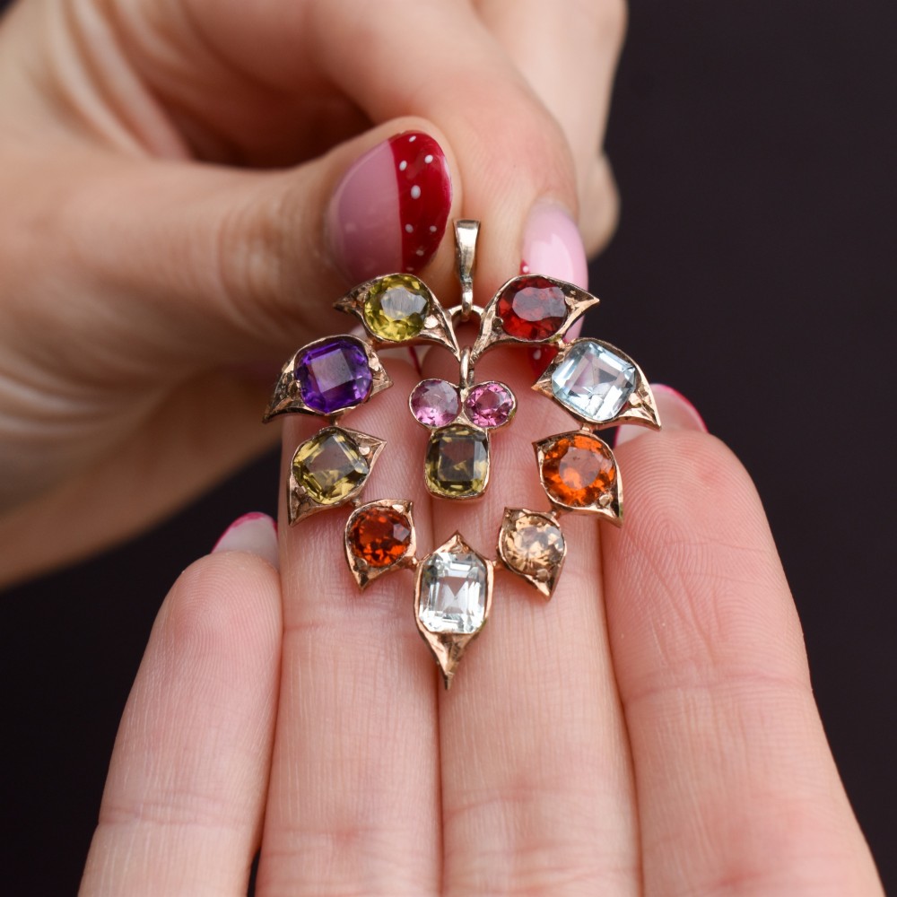 An antique 9ct yellow gold floral drop pendant composed of leaf-shaped settings encasing various multi-coloured faceted gemstones. View VIII