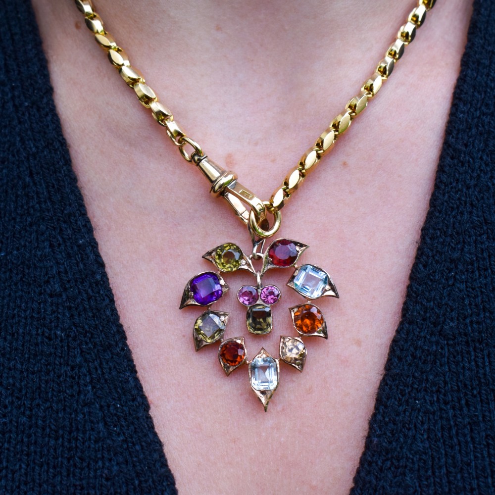 An antique 9ct yellow gold floral drop pendant composed of leaf-shaped settings encasing various multi-coloured faceted gemstones. View X