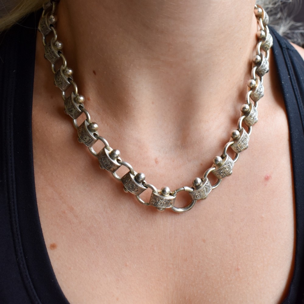 An antique Victorian sterling silver collar necklace featuring wide engraved rectangular links accented with silver beads and linked by circular rings. View V