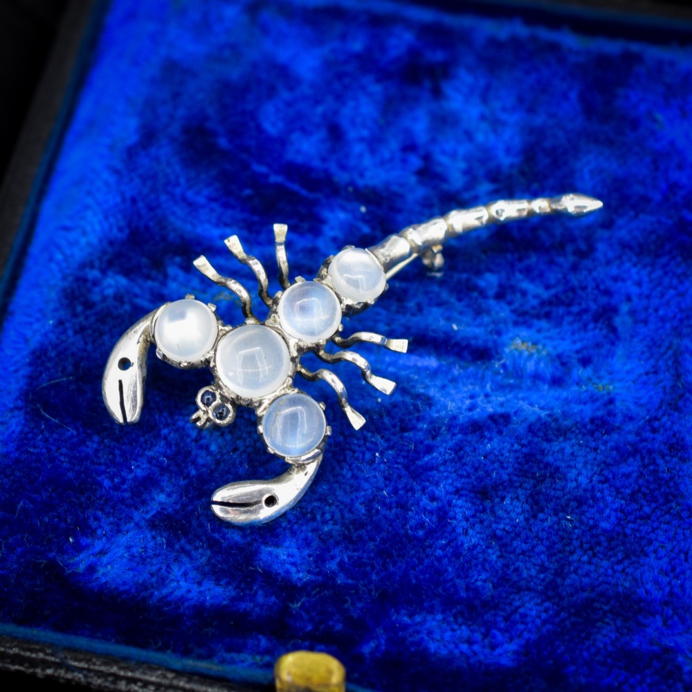 An antique silver scorpion brooch set with five circular cabochon moonstones along its body.