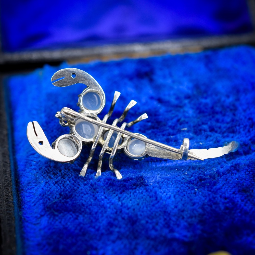 An antique silver scorpion brooch set with five circular cabochon moonstones along its body. View VI