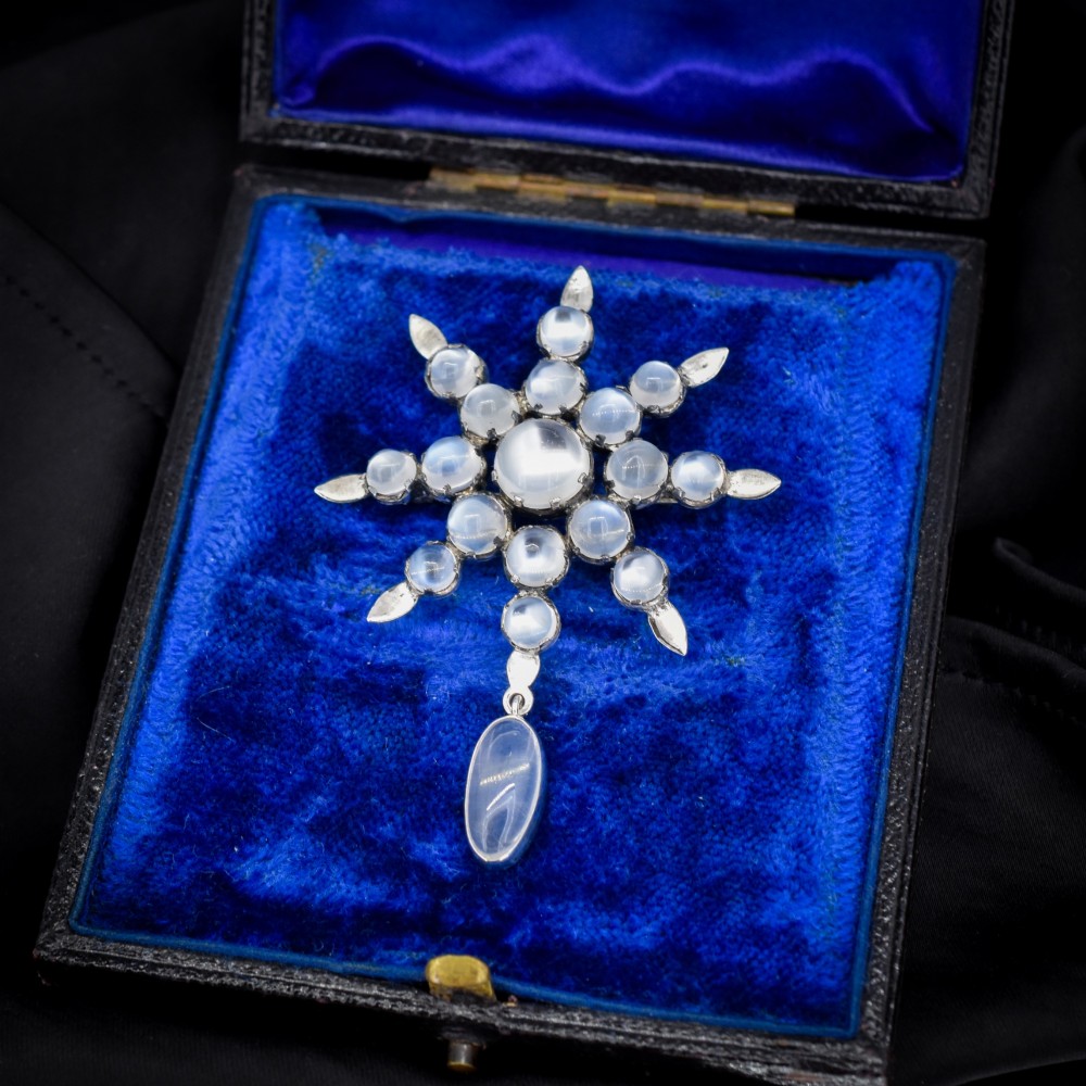 A Victorian silver starburst brooch set with round cabochon moonstones and a suspended oval moonstone drop.