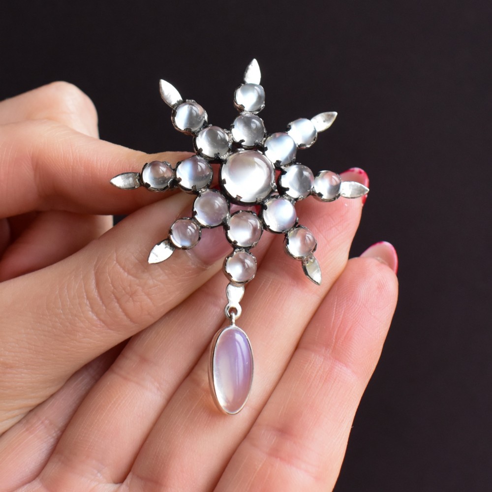 A Victorian silver starburst brooch set with round cabochon moonstones and a suspended oval moonstone drop. View VIII