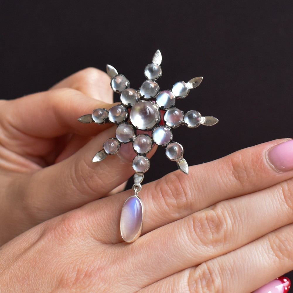 A Victorian silver starburst brooch set with round cabochon moonstones and a suspended oval moonstone drop. View IX